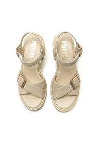 Beige Sandalen mit einem glatten synthetischen Obermaterial, überkreuzten Riemen, verstellbarem Knöchelverschluss und einer dicken Sohle mit einem leichten Absatz.