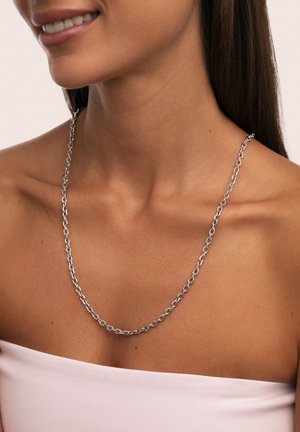 Collier en chaîne argentée avec des maillons ovales, présenté sur une peau nue. La chaîne est de largeur moyenne avec une finition polie.