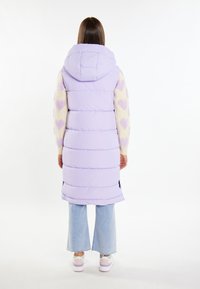 Lavendelkleurige puffer-vest met een capuchon, gestikt ontwerp en zijsplitten, gecombineerd met lichtblauwe flare jeans en witte sneakers.