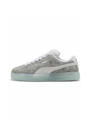 Baskets basses en daim gris Puma avec une bande blanche, des lacets blancs et une semelle en caoutchouc translucide, vues de côté.