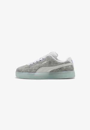 Baskets basses en daim gris Puma avec une bande blanche, des lacets blancs et une semelle en caoutchouc translucide, vues de côté.