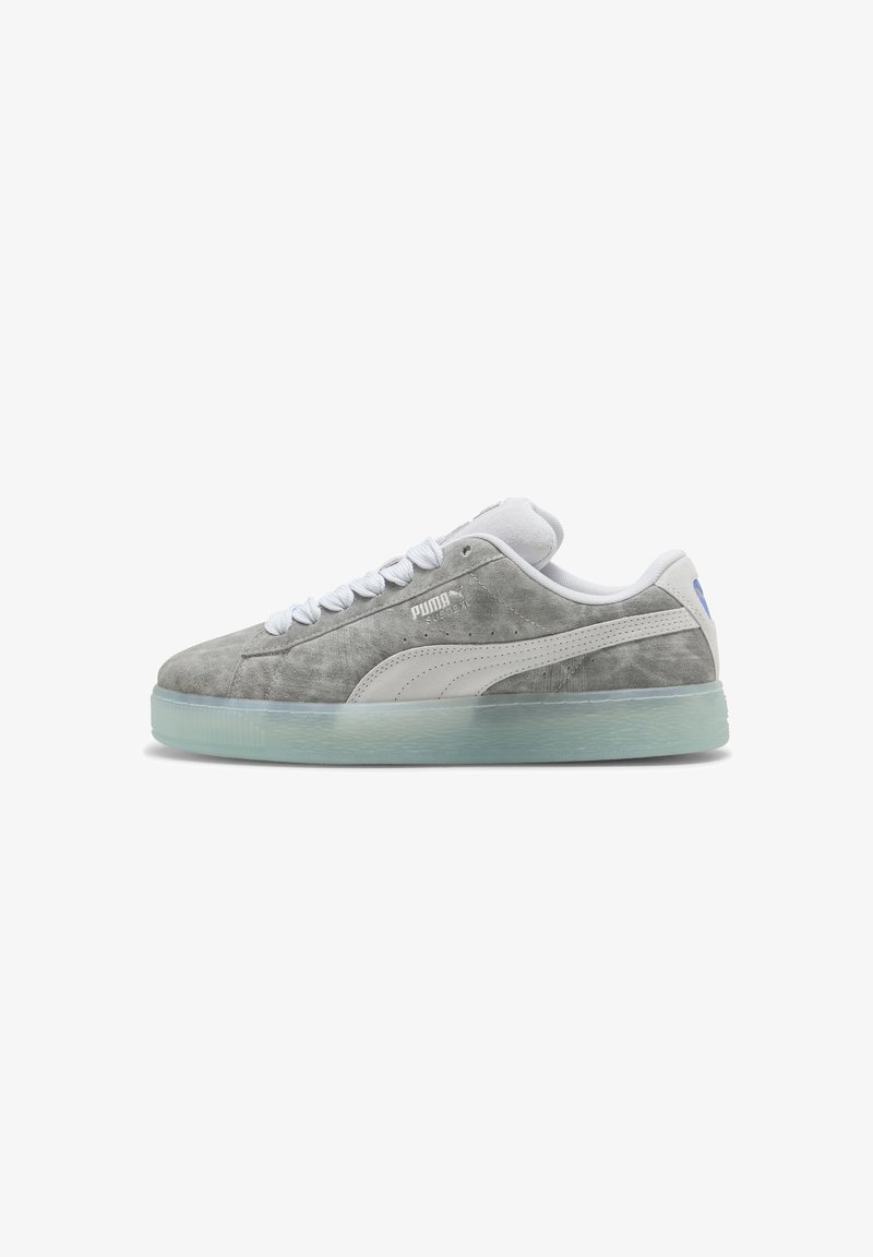 Baskets basses en daim gris Puma avec une bande blanche, des lacets blancs et une semelle en caoutchouc translucide, vues de côté.