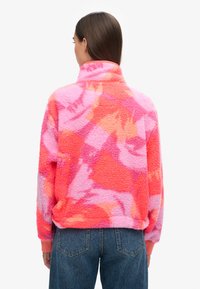 Fleece-trøje i pink og orange abstrakt mønster med høj krave og elastiske manchetter; blød tekstur, afslappet pasform, levende farvekontrast.