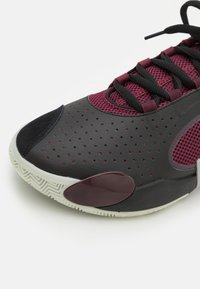 Zwarte en bordeauxrode sneaker met geperforeerde bovenkant, mesh tong, ronde neus en rubberen zool met een visgraatpatroon.