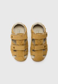 Sandales en cuir marron avec des bandes Velcro, des détails perforés et des coutures contrastées. Design ouvert à l'avant avec un intérieur rembourré.