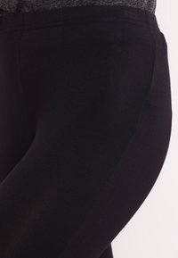 Svarta tights i elastisk tyg, med en slät yta och en figurnära design, samt ett elastiskt midjeband för komfort.