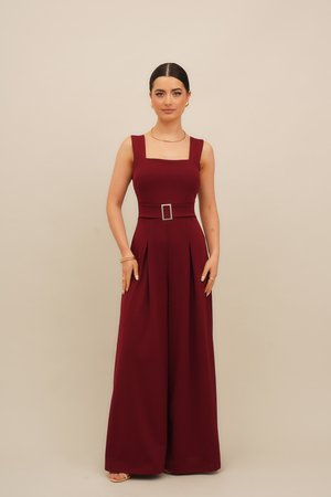 Burgundy jumpsuit with a square neckline, wide leg, and pleats, featuring a belted waist and a silver buckle accent. Smooth, thick fabric.