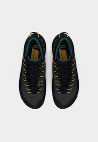 Μαύρα και γκρι υποδήματα με υφή στην επιφάνεια, κορδόνια κίτρινα και τυρκουάζ, στρογγυλοποιημένη μύτη και ενισχυμένη καουτσούκ σόλα για ανθεκτικότητα.