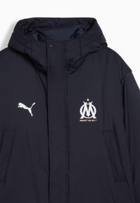 Veste à capuche bleu marine avec poches avant, logo Puma sur la poitrine droite, emblème du club de football de Marseille et texte « Droit Au But » sur la poitrine gauche.