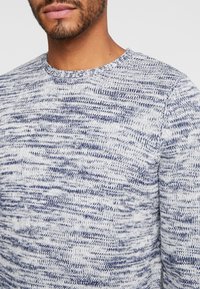 Stickad tröja i ljusgrått med marinblå prickigt mönster. Har rund halsringning och strukturerad tyg. Avslappnad passform, perfekt för lager-på-lager. 