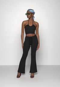 Top preto cropped com alças finas, combinado com calças pretas largas, apresentando uma cintura ajustável por cordão. Os acessórios incluem óculos de sol verdes e um lenço azul.