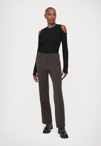 Top negru cu maneci lungi, cu decupaje la umeri și textură cu nervuri, combinat cu pantaloni maro cu dungi. Modelul poartă încălțăminte chunky neagră.