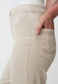 Pantaloni in cotone beige con vestibilità slim, dettagli delle tasche frontali e una texture liscia, che mettono in evidenza le cuciture lungo i lati.
