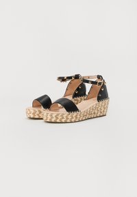 Sandales en cuir noir à talon compensé avec une ouverture à l'avant, une bride autour de la cheville, des clous en forme de pyramide dorés et une semelle en jute tissée.