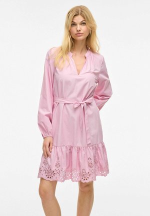 Rosa klänning med långa ärmar, v-ringning, bälte i midjan och volangslut med utskurna blommönster. Slät tygkänsla.