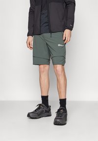 Lette, grønne shorts med slim fit og frontlommer. Kombinert med grå joggesko og svarte sokker, perfekt for utendørsaktiviteter.