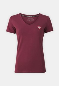 Burgundin värinen V-kaula-aukkoinen t-paita, joka on valmistettu luomupuuvillasta. Vasemman rinnan alueella on pieni kolmion muotoinen logo-patch. Lyhyet hihat.