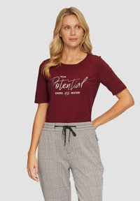 Bordeaux T-shirt met korte mouwen met zilveren tekst "Je potentieel kent geen grenzen." Gepaard met geruite broek met elastische tailleband.