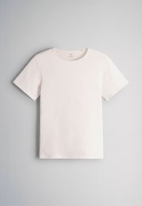 T-shirt blanc uni à manches courtes et col rond, posé à plat sur un fond gris clair, montrant le devant et la texture lisse du tissu.