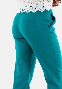 Pantalons ajustés bleu canard en tissu lisse avec un design ajusté, dotés de poches latérales et d'un détail de couture subtil.