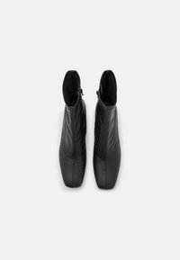 Černé kožené kotníkové boty s elegantním designem, špičatou špičkou a zipovým zapínáním na zadní straně. Hladký povrch s jemným prošíváním.