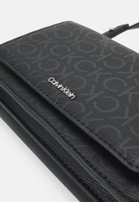 Czarny portfel Calvin Klein z wytłoczonym wzorem logo i srebrną nazwą marki na teksturowanej powierzchni skóry syntetycznej.
