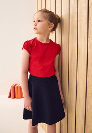 Rotes Baumwoll-T-Shirt mit kurzen Puffärmeln, kombiniert mit einem schwarzen ausgestellten Rock, beide mit glatten Texturen vor einem hölzernen Hintergrund.