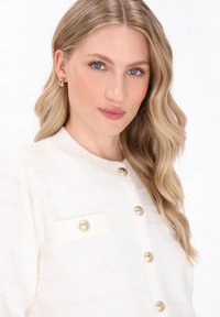 Cardigan bianco con texture, bottoni dorati e tasca applicata. Presenta un colletto a coste e un tessuto a maglia morbido.