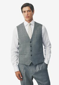 Grau melierte Weste aus Wollmischung mit strukturiertem Finish, sechs Knöpfen und zwei Fronttaschen, kombiniert mit einem weißen Hemd und einer gepunkteten Krawatte.