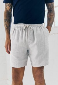 Shorts en lin gris clair avec un waistband élastique et un cordon de serrage, dotés de poches latérales et d'une coupe décontractée.