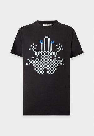 Mand stående iført en sort T-shirt med et pixel-art krabbe motiv og løstsiddende mørkeblå ternede bukser med sorte sko.