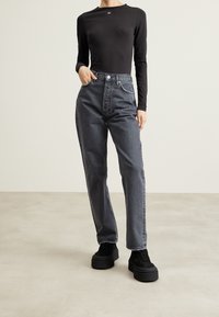 Top nero a maniche lunghe abbinato a jeans grigio scuro a vita alta. I jeans presentano una gamba dritta, tasche frontali e dettagli di cucitura discreti.
