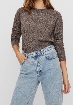 Pull marron texturé à manches longues, associé à un jean taille haute bleu clair avec un effet délavé et une fermeture à boutons sur le devant.