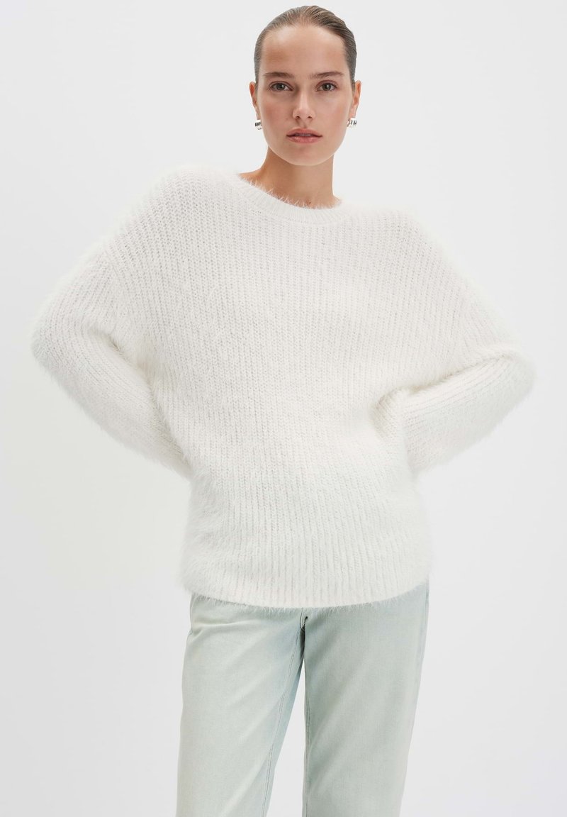 Witte, fluffy gebreide trui met verlaagde schouders en een ontspannen pasvorm. Gestyled met lichtgekleurde, rechte jeans. Zachte, gestructureerde stof.