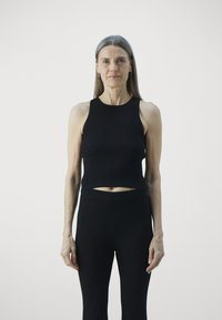 Top corto a righe nera con scollatura rotonda abbinato a leggings neri attillati, texture liscia e design minimal. 