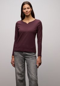 Top w kolorze głębokiego bordo z długim rękawem, o prążkowanej strukturze i dekoltem w serek, zestawiony z szarymi dżinsami o szerokich nogawkach.