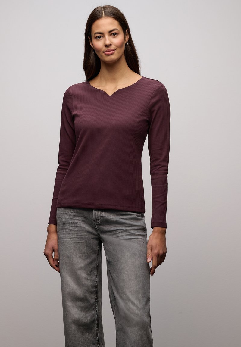 Top w kolorze głębokiego bordo z długim rękawem, o prążkowanej strukturze i dekoltem w serek, zestawiony z szarymi dżinsami o szerokich nogawkach.