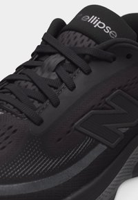 Κοντινό πλάνο ενός μαύρου παπουτσιού τρεξίματος New Balance με υφασμάτινη υφή, μαύρα κορδόνια και την επιγραφή «ellipse» στη γλώσσα.