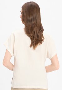 Crème-kleurige top met korte mouwen, voorzien van een losse pasvorm en een ronde halslijn, gemaakt van lichtgewicht stof met een zachte textuur.