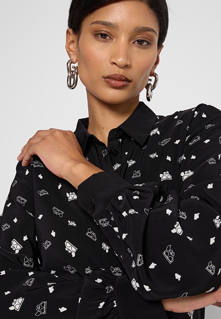 Camisa negra con ilustraciones blancas divertidas de gafas y coronas, con diseño de cuello y cierre de botones. Tela suave y texturizada.