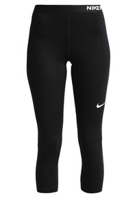 Leggings de sport courts noirs avec un swoosh blanc Nike sur la cuisse et le logo Nike sur la ceinture.