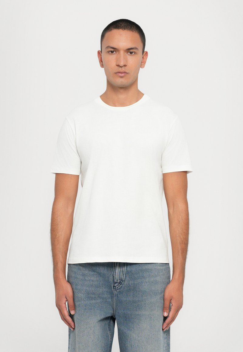Valge puuvillane T-särk lühikeste varrukatega, ümmarguse kaelusega ja vabalt langev, koos helesiniste denim teksadega. Minimalistlik disain, ilma mustriteta.