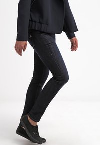 Jeans ajustados en denim índigo oscuro, con una silueta ceñida, un sutil desgaste y detalles de costura. Combinados con zapatillas negras.