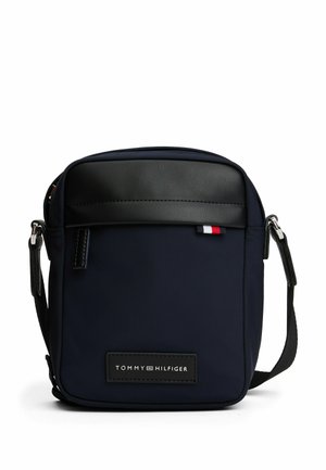 Bandolera azul marino con parte superior de cuero sintético negro, correa ajustable y parche con el logo. Presenta una textura suave y cierre de cremallera.