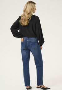 Juoda ilgomis rankovėmis palaidinė, mėlyni aukšto liemens tiesaus kirpimo džinsai, lygus audinys, penki kišeniai, nematomi raštai, dėvimi su juodais aukštakulniais batais.