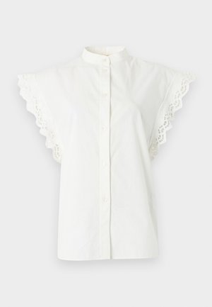 Valge lühikeste varrukatega pluus kõrge krae, ees nööpidega ja varrukatel volangiline pitsääris, taustaks ühtlane taust.