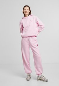 Rosa hettegenser med frontlomme og lite hjerte-logo, kombinert med matchende rosa joggebukser. Begge laget av myk stoff, med elastiske mansjetter.