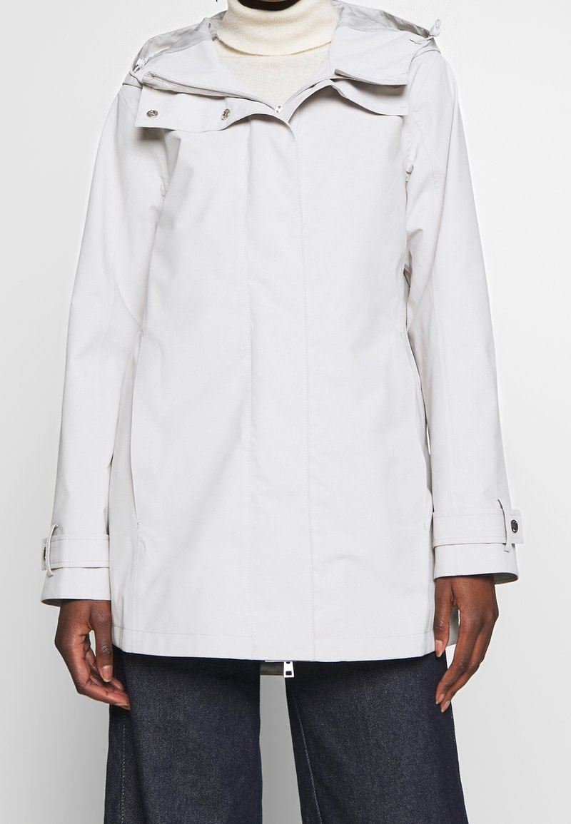 Světle šedá nepromokavá bunda se zipovým zapínáním, nastavitelnou kapucí a knoflíkovými manžetami. Disponuje bočními kapsami a hladkým, strukturovaným povrchem.