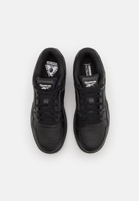 Black athletic sneakers featuring leather material, perforated toe box, flat laces, and padded collar. Logo prominently displayed on tongue.