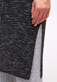 Käsi lepab musta ja halli tekstuuriga kangal, millel on külgsisselõige, näidates kahte kihti riideid ribakujunditega.